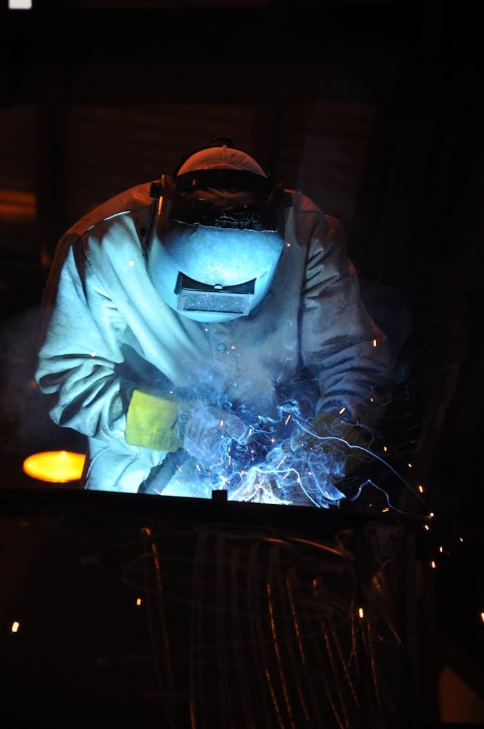 hero-img-01 A skilled welder working in a dark workshop with blue sparks flying, showcasing metalworking expertise.